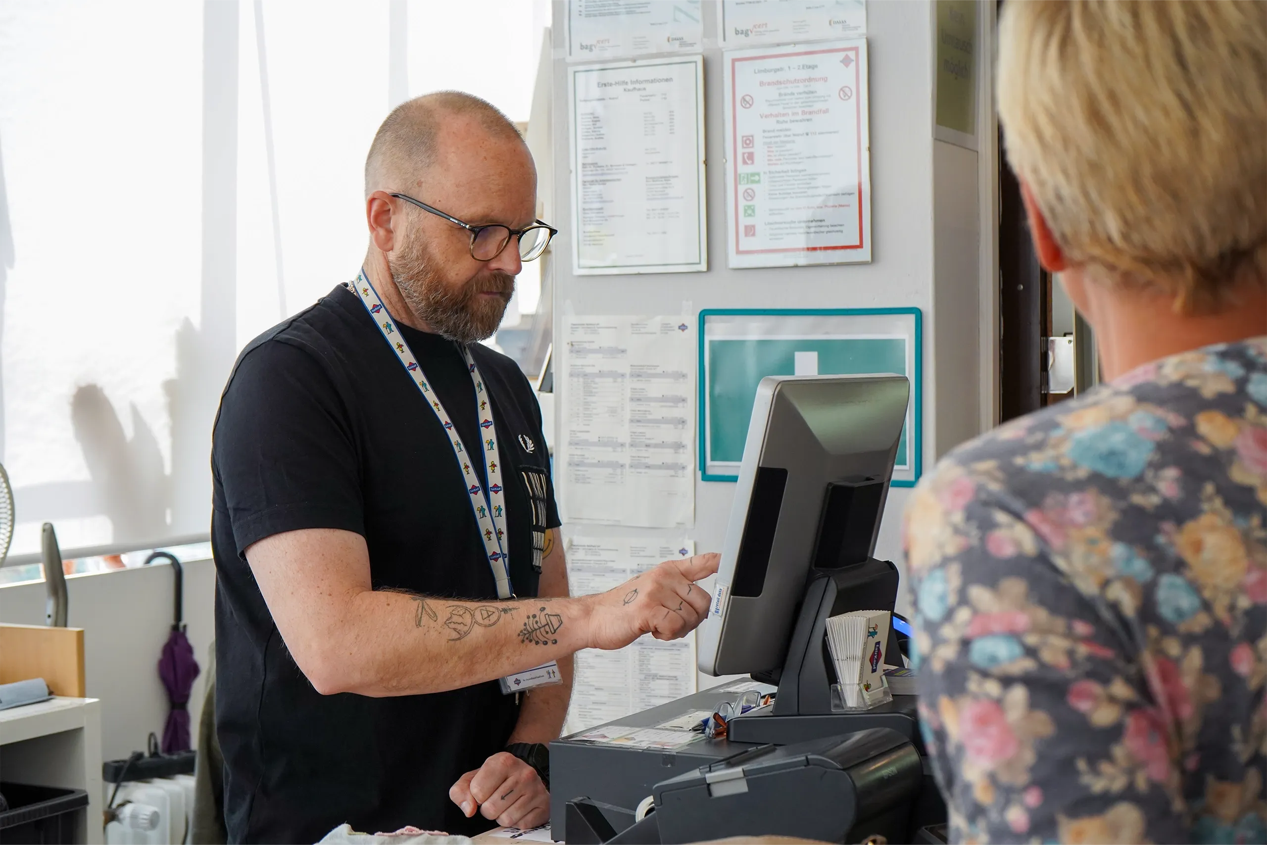 Ein Mitarbeiter an einer Kasse bedient einen Kunden in einem Verkaufsraum.