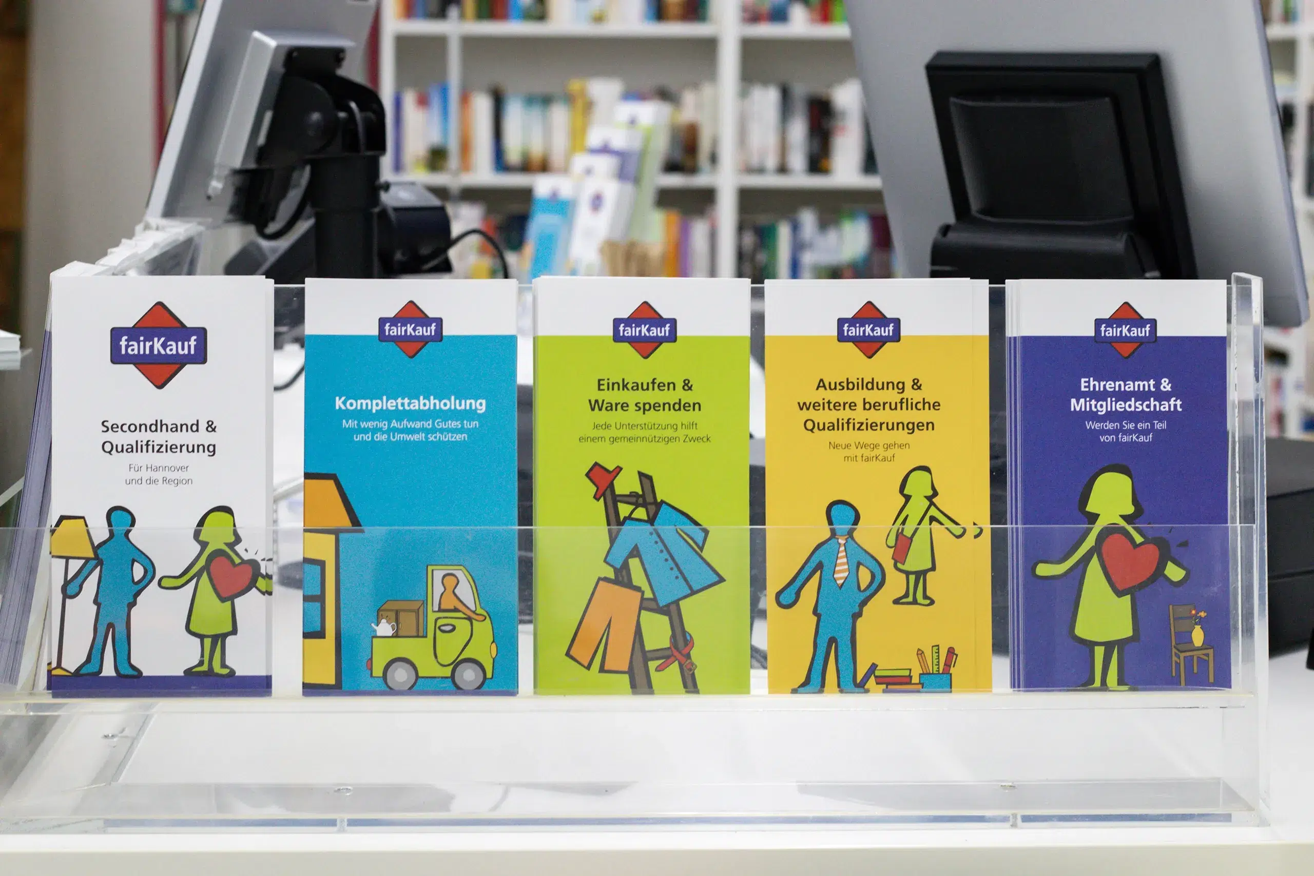Verschiedene Informationsflyer von fairKauf zu Themen wie Secondhand, Komplettabholung, Spenden und ehrenamtlichen Tätigkeiten stehen in einem Präsentationsständer.