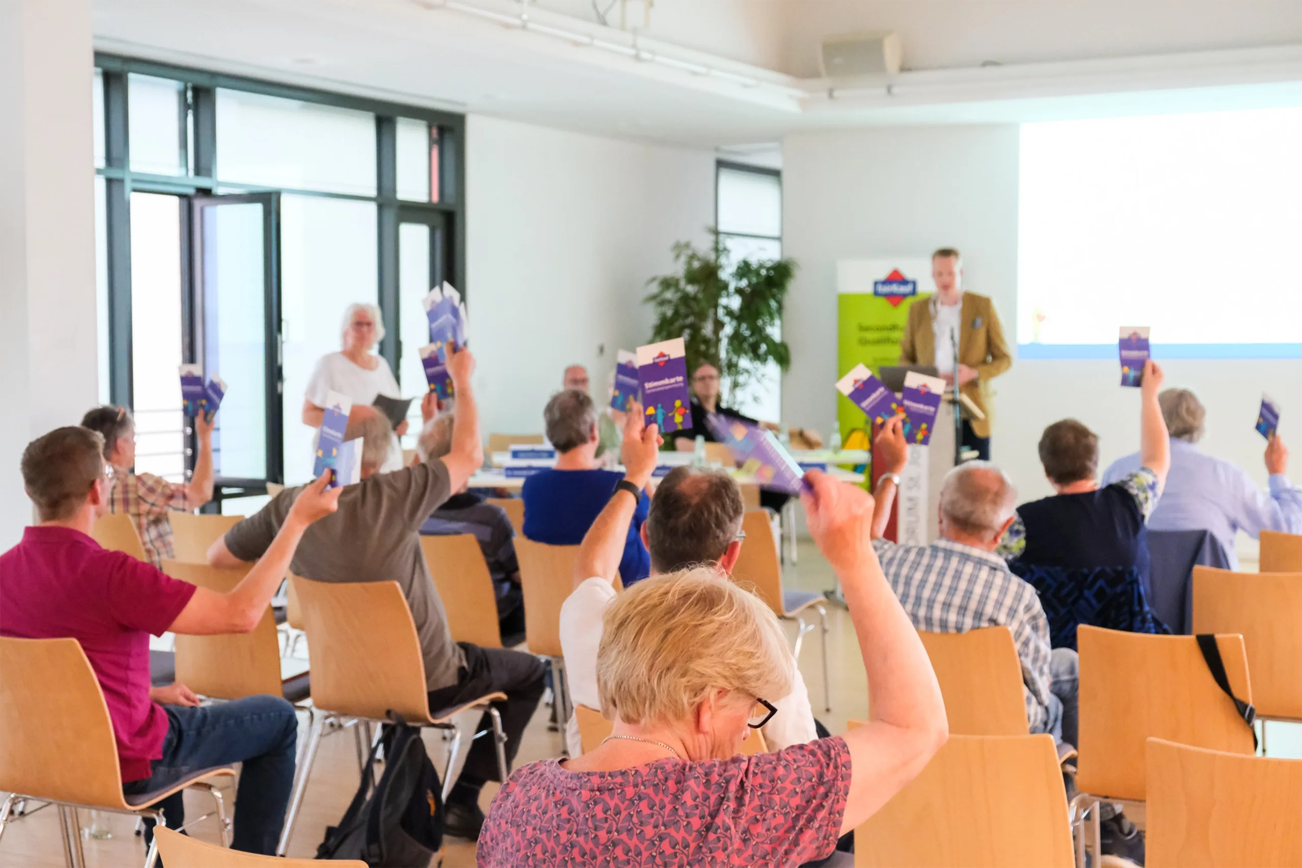 Teilnehmer einer Mitgliederversammlung heben ihre Stimmzettel zur Genehmigung von Beschlüssen.