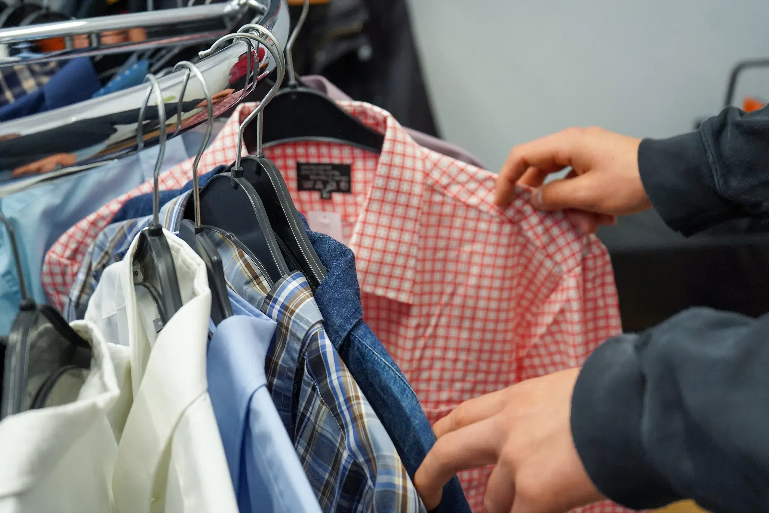 Eine Person untersucht verschiedene Hemden an einem Kleiderständer in einem Bekleidungsgeschäft.